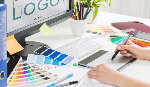 designing logo on pad in front of computer with many colour swatches on desk