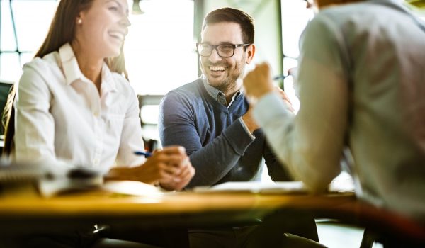 Young happy couple communicating with their financial advisor on a meeting in the office. Focus is on man.